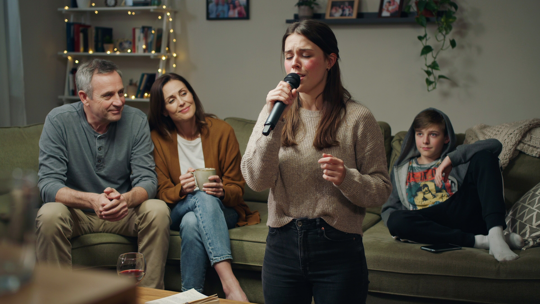A girl is singing shyly in front of her family in her living room.