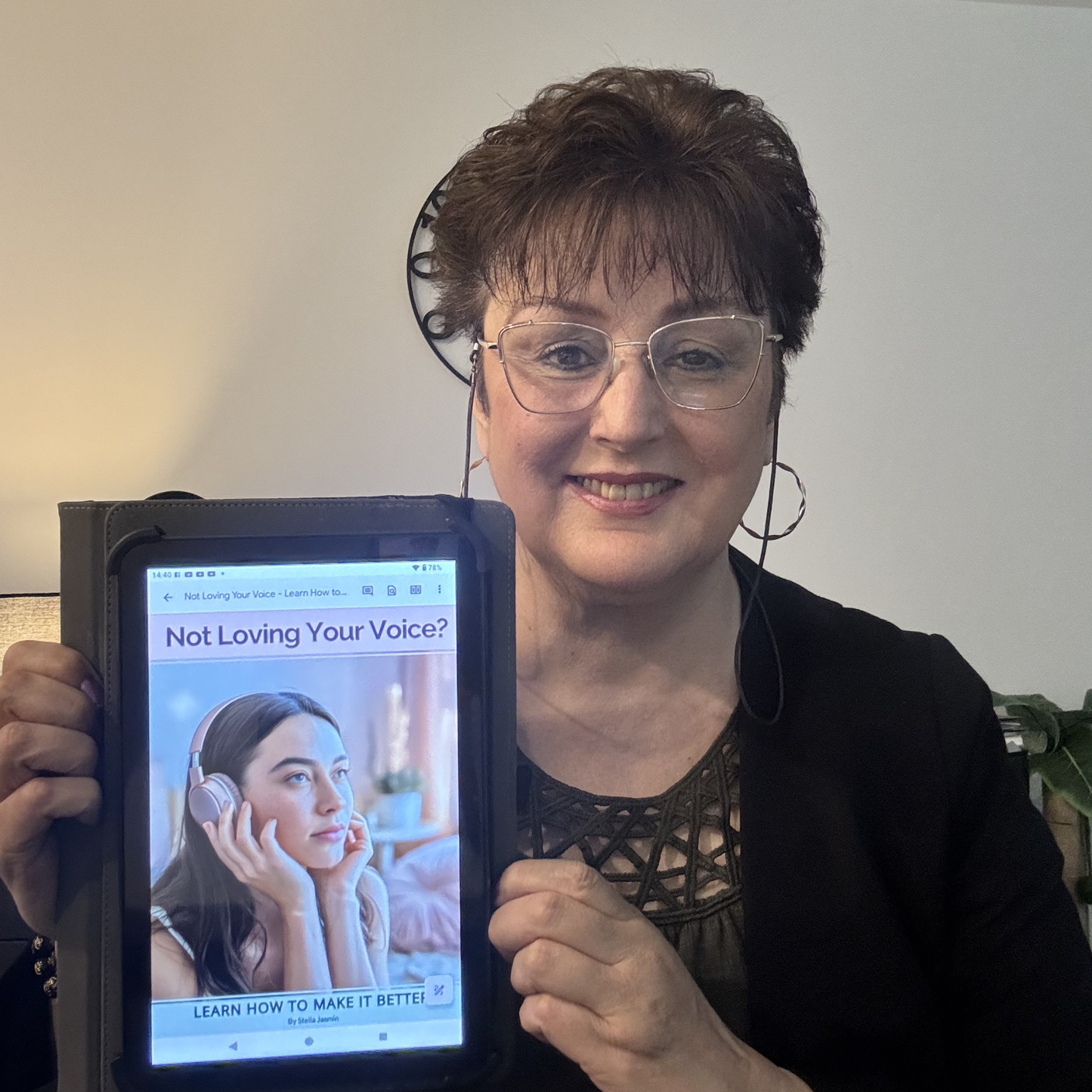 Stella Jasmin holding a tablet with a screen displaying the e-book, 'Not Loving Your Voice? Learn How to Make It Better'.