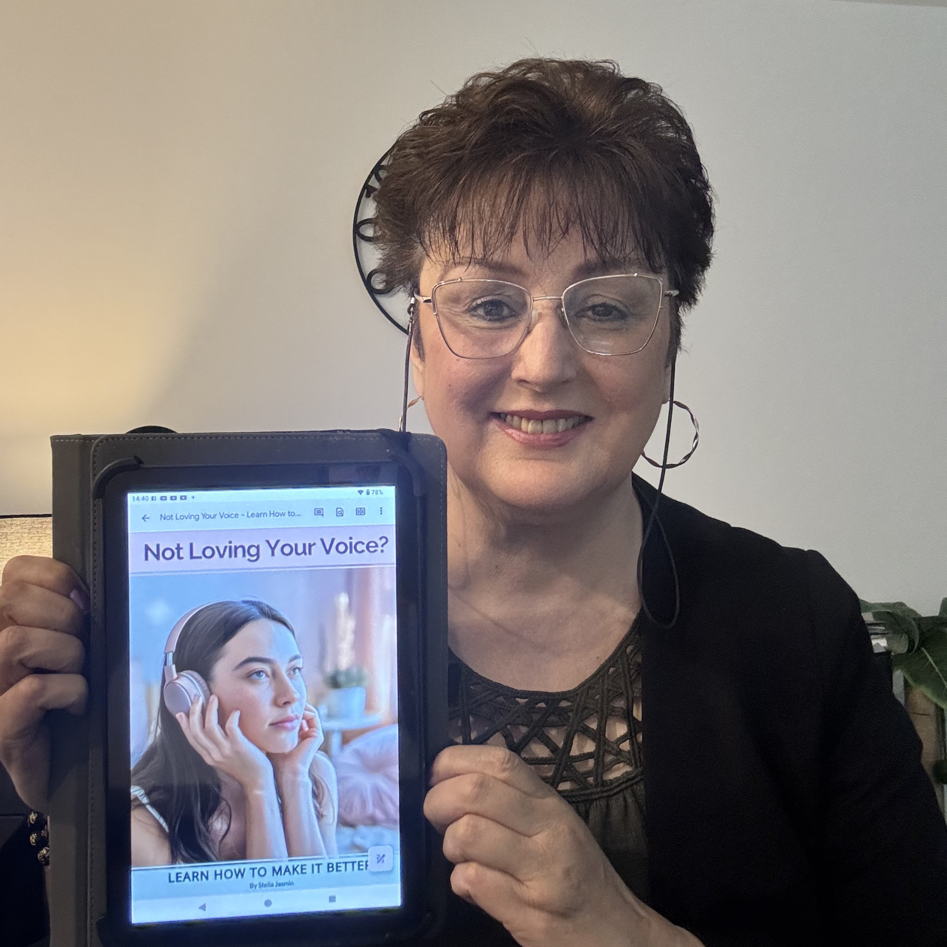 Stella Jasmin holding a tablet with a screen displaying the e-book, 'Not Loving Your Voice? Learn How to Make It Better'.